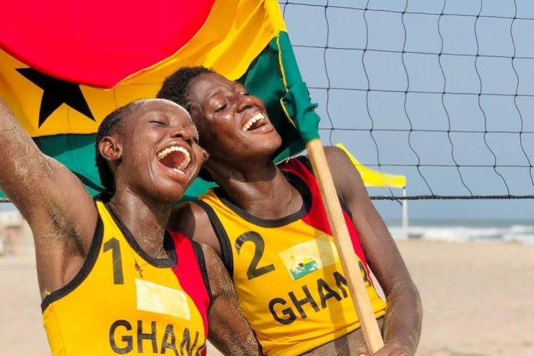 "Smiling beach volleyball players holding a Ghana flag."