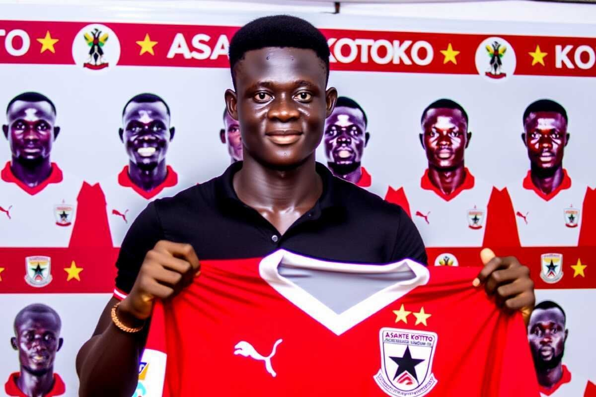 A football player proudly holding an Asante Kotoko jersey during his unveiling, with the team's logo and branding in the background."