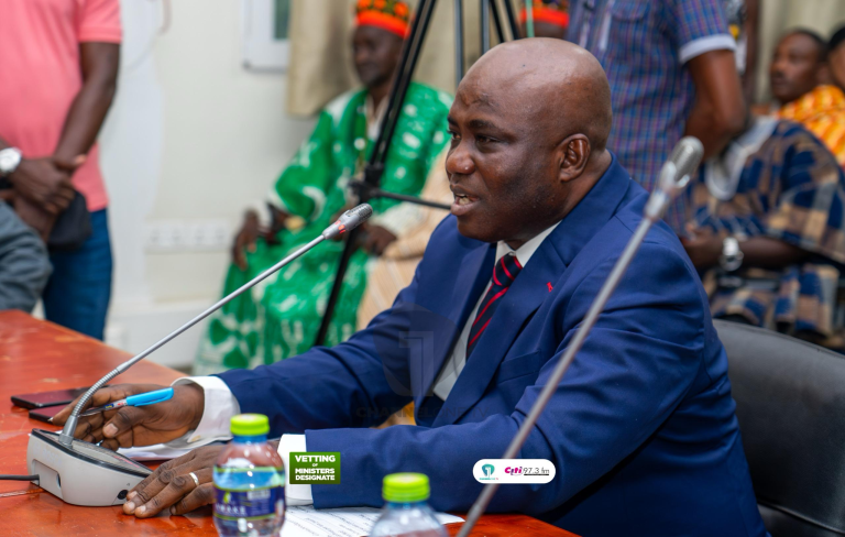 "Man in a suit speaking into a microphone during an official meeting."