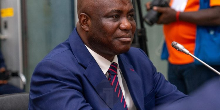 "Man in a navy suit attending an official event, seated and listening attentively."