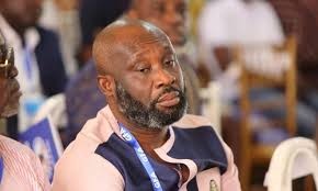 "George Afriyie wearing a patterned shirt, seated and listening attentively during an event."