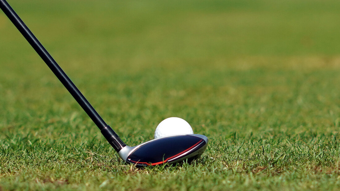 A close-up of a golf club positioned next to a golf ball on a grassy course.