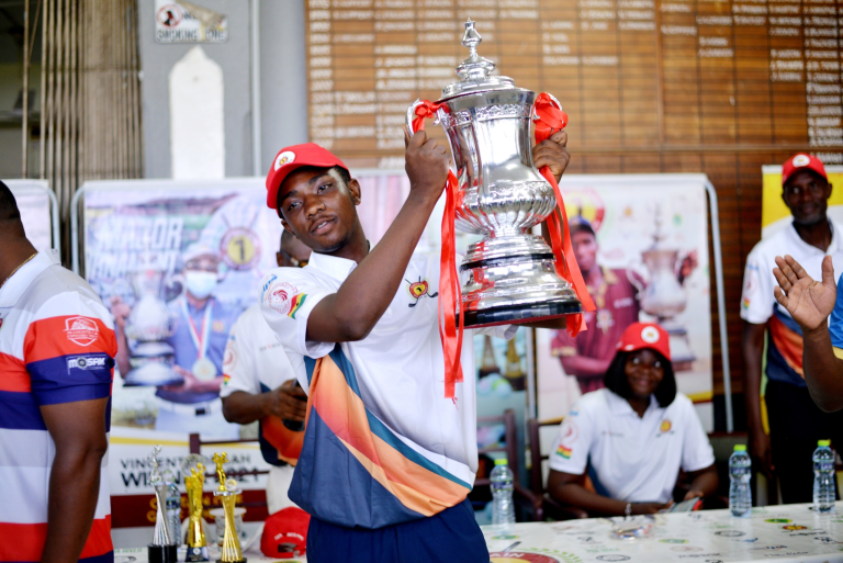 A person wearing a red cap and sports attire holds up a large silver trophy in celebration.