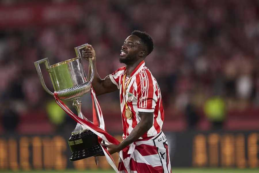 Football player in red and white jersey celebrating with a trophy.