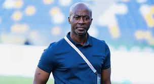 "Coach Ibrahim Tanko wearing a blue shirt, standing on a football field."