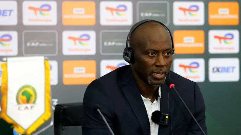 "Coach Ibrahim Tanko wearing headphones, addressing a press conference with CAF branding in the background."