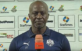 "Coach Ibrahim Tanko in a navy-blue shirt, holding an orange microphone during a post-match interview."