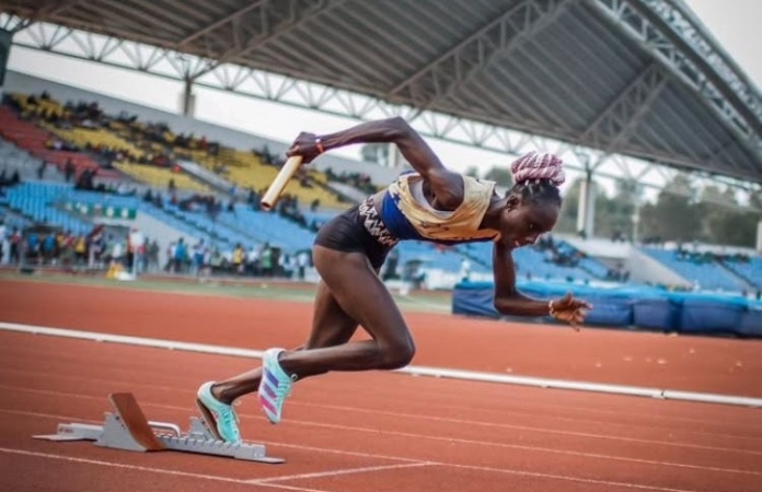 Female athlete sprinting in a relay race at a stadium.