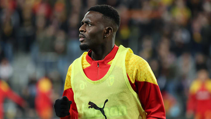 A football player wearing a yellow training bib over a red and yellow Puma jersey during a warm-up session.