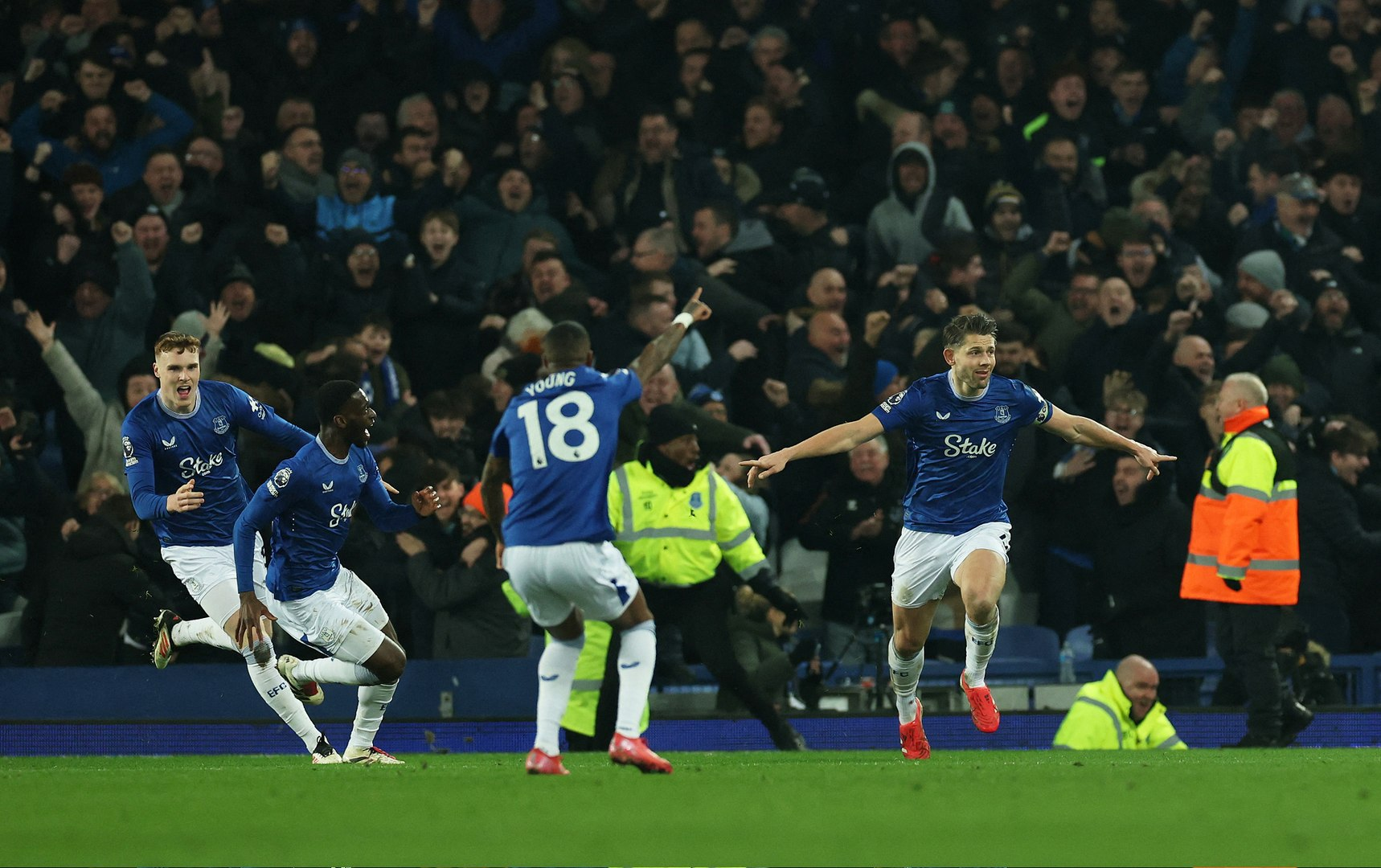 vigo3 Everton football players celebrating a goal on the field with fans in the background.