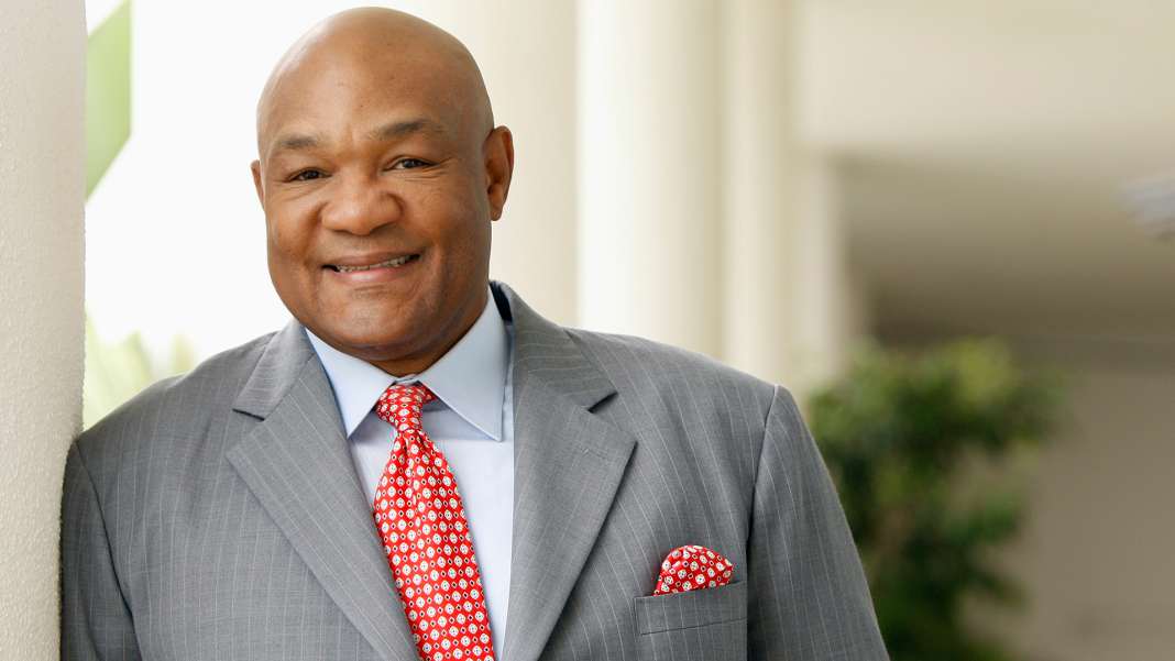 George Foreman smiling in a grey suit with a red tie.