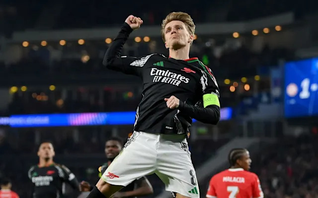 a soccer player from Real Madrid is celebrating during a match. He's wearing the team's black away kit with white accents, and his expression and raised fist suggest he is celebrating a goal or a decisive moment in the game.