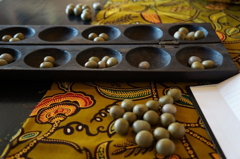 Traditional Oware board game with seeds on a colorful African fabric background.