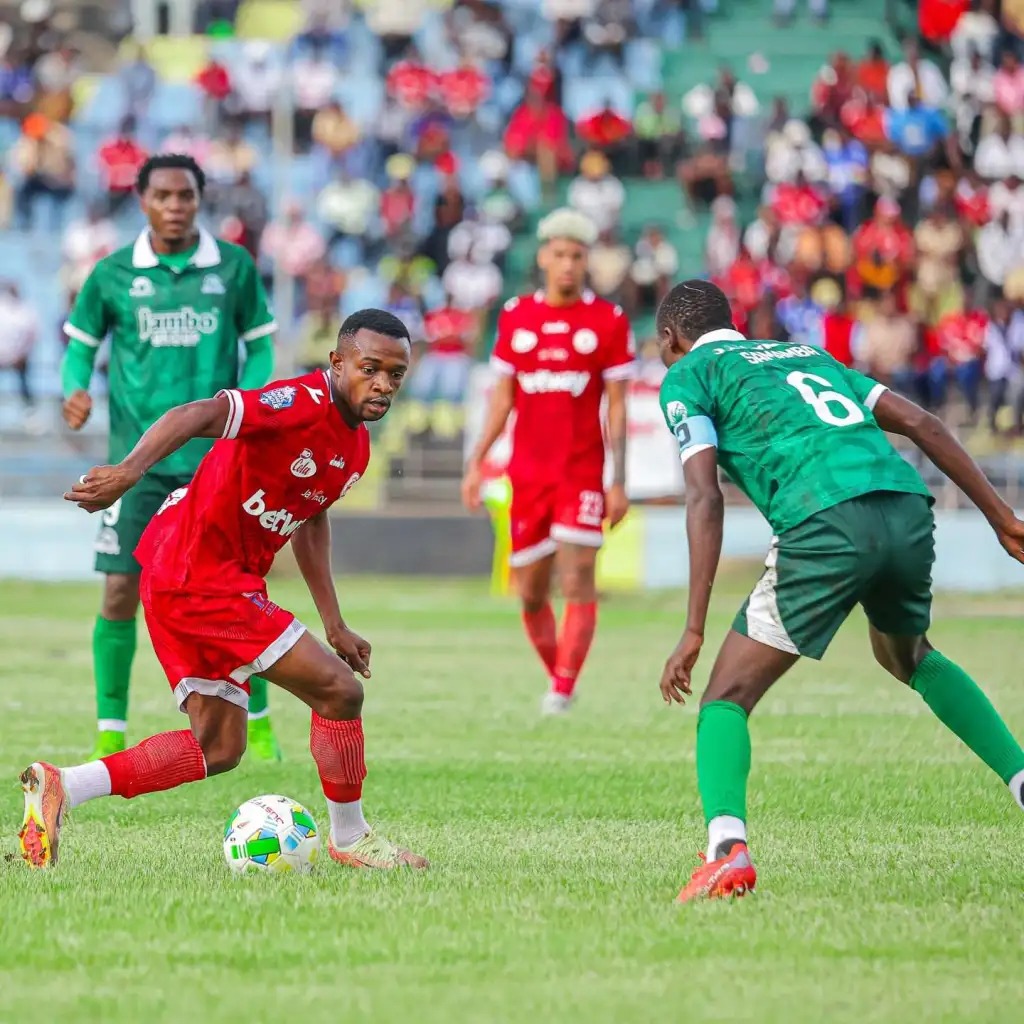 Ellie Mpanzu Akidhibiti Mpira Mbele ya Beki wa Pamba Jiji FC Mchezaji wa Simba SC Ellie Mpanzu akiwa na mpira mguuni akijiandaa kumchenga beki wa Pamba Jiji FC wenye jezi ya kijani.
