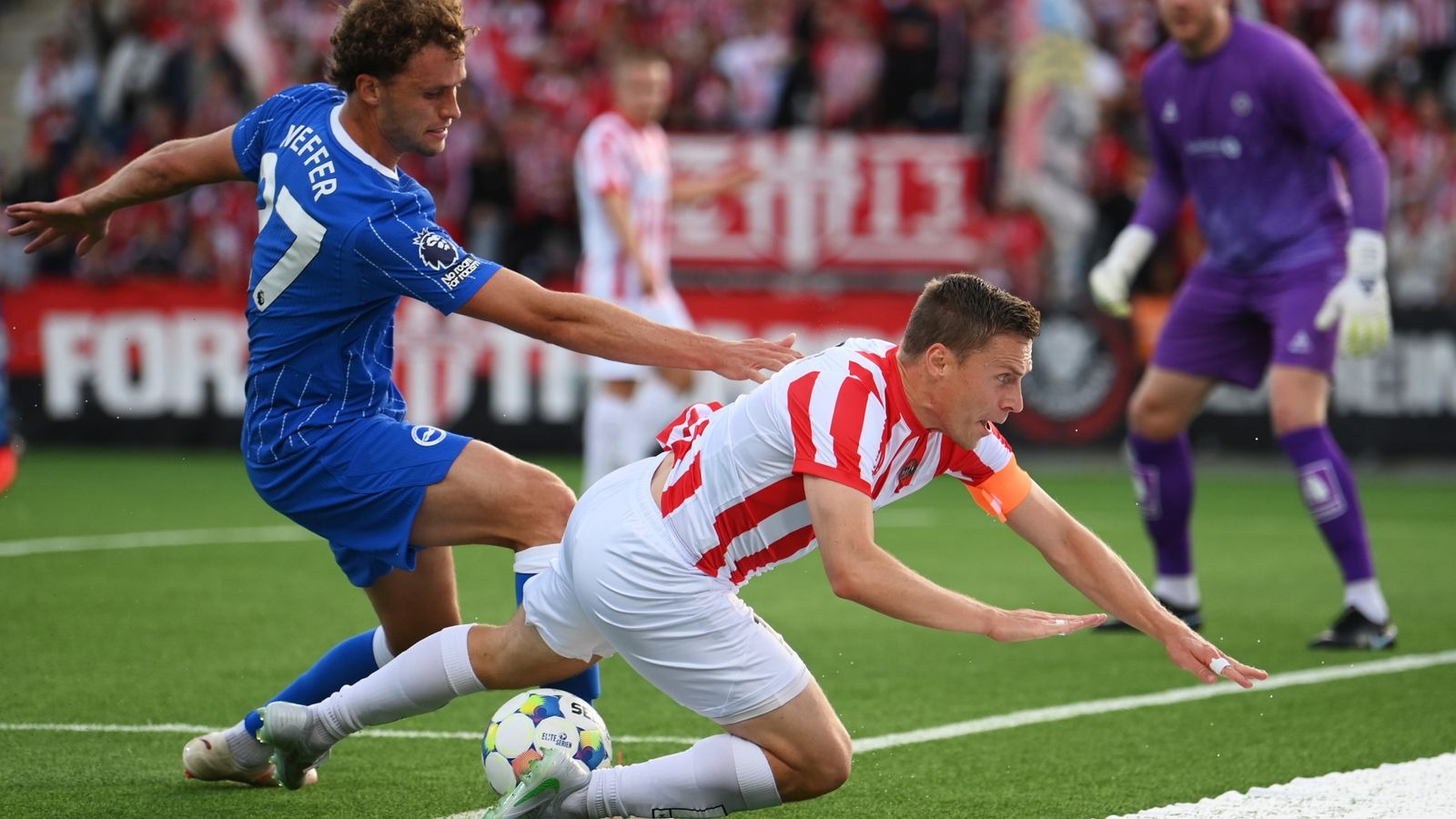 Mats Wieffer Akitaka Kunyanya Mpira dhidi ya Tromsø Mats Wieffer wa Brighton mwenye jezi ya bluu akimzuia mchezaji wa Tromsø aliyesogea chini kuwania mpira uwanjani.