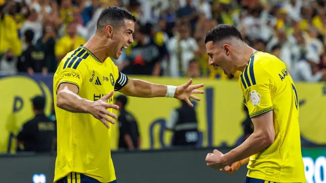 Cristiano Ronaldo akiwa amevalia jezi ya njano ya Al-Nassr akishangilia kwa furaha uwanjani pamoja na mchezaji mwenzake.