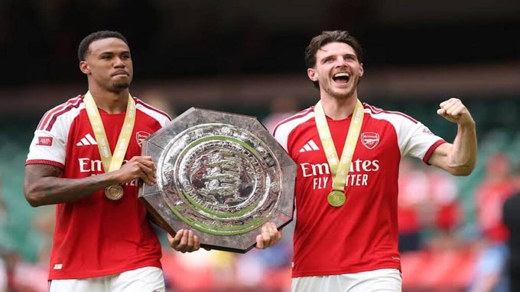 Arsenal players Gabriel Magalhães and Declan Rice hold the Community Shield trophy while wearing medals during the club’s title celebrations.