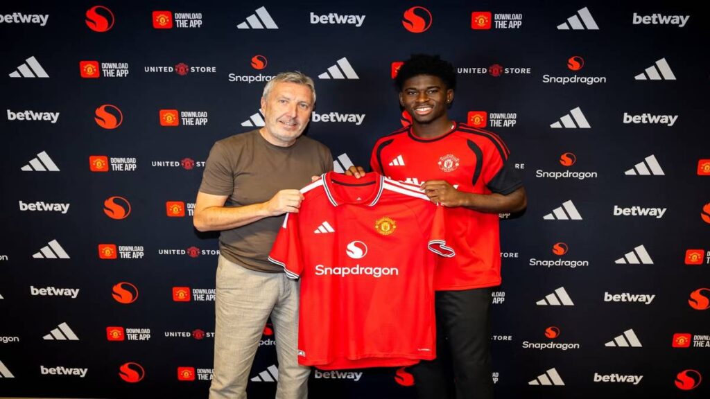 Carlos Baleba poses with a Manchester United official while holding the club shirt during his unveiling ceremony.