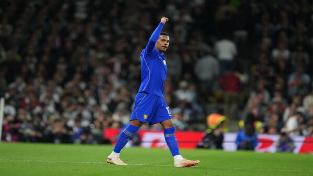 Chelsea player Rogers in a blue kit raises his fist in celebration after scoring during a Premier League match.