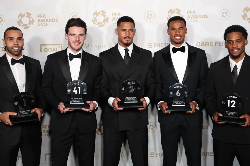 Arsenal players dressed in black suits hold PFA Premier League Team of the Year trophies during the 2026 PFA Awards event.