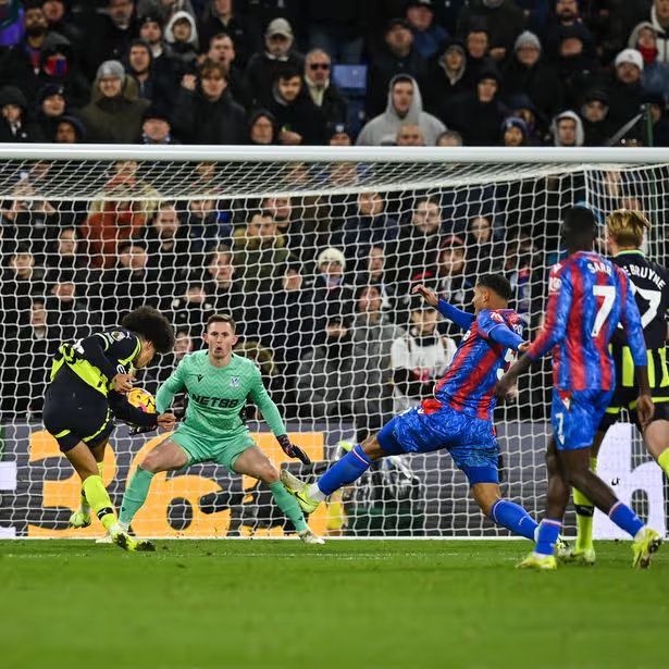 Manchester City player shoots at goal while the Crystal Palace goalkeeper and two defenders guard the penalty area.