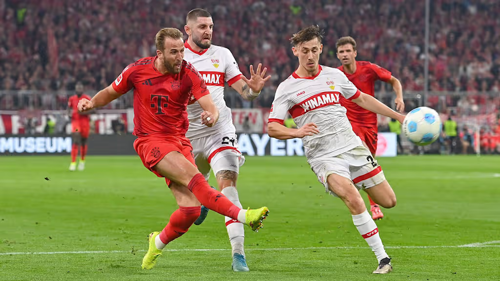 Harry Kane shoots with his left foot as two Stuttgart defenders attempt to block him inside the penalty area.