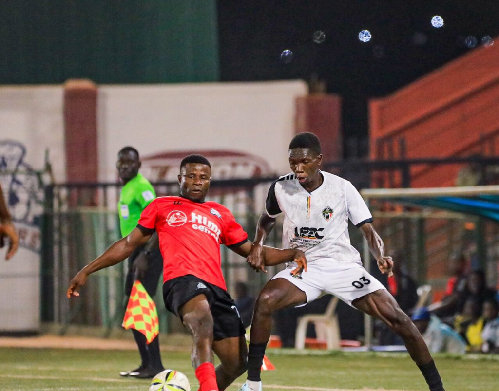 Vipers player in red challenges an Entebbe UPPC player in white for the ball during a night match.