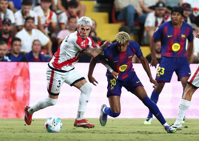 Barcelona winger Lamine Yamal shields the ball while being challenged by a Rayo Vallecano defender.