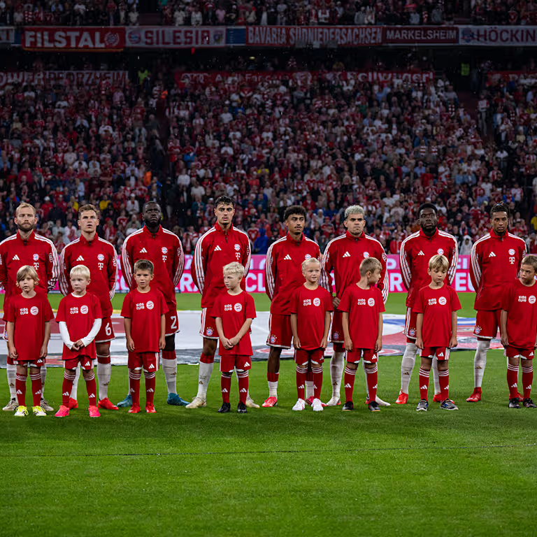 Bayern Munich’s starting players stand alongside young mascots before kick-off at the Allianz Arena.