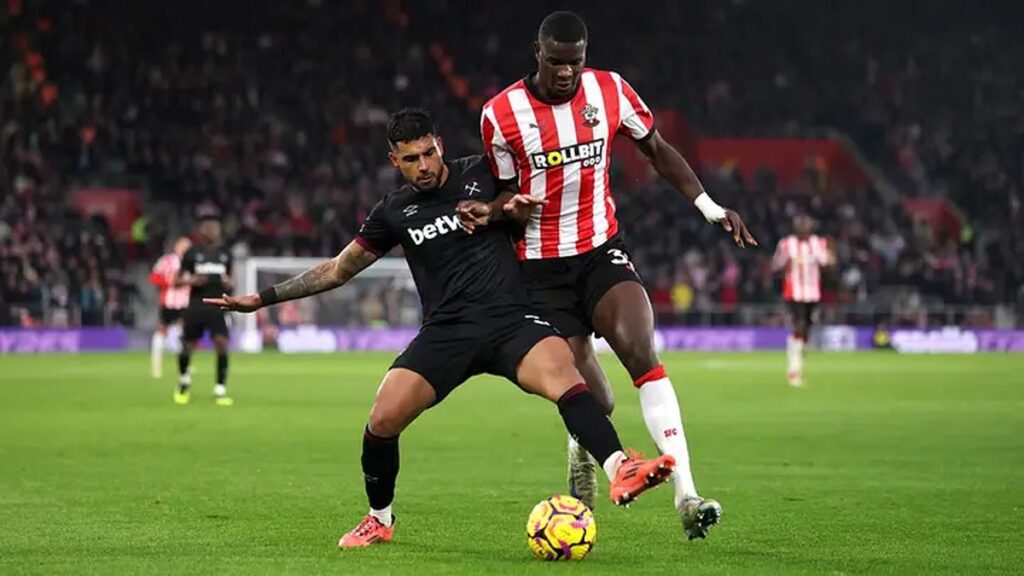 Southampton player in red-and-white stripes battles with a West Ham player in black kit for the ball during a football match.