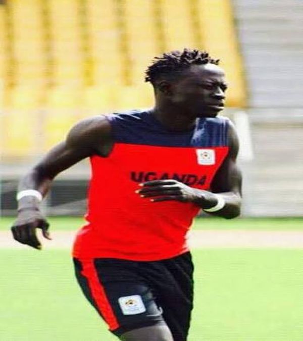 Uganda football player wearing a red and black national team training kit runs during a training session on the pitch.