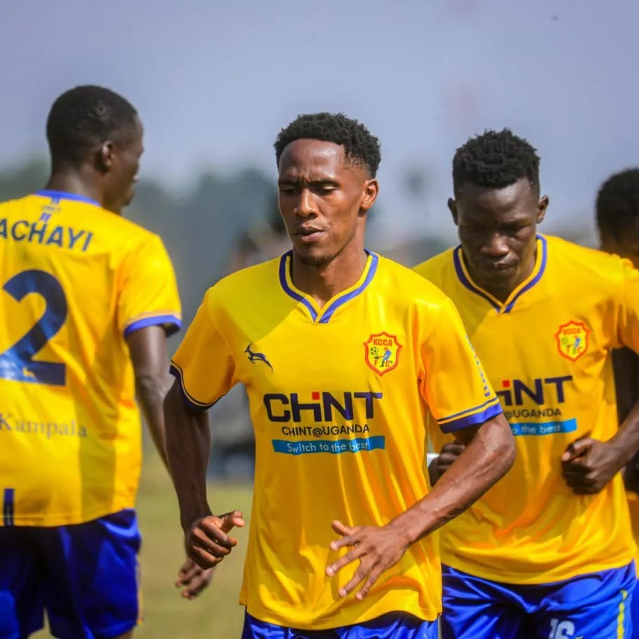 Group of KCCA FC football players wearing yellow jerseys with blue trim, sponsored by CHINT, jogging together on a pitch during pre-match warm-up.