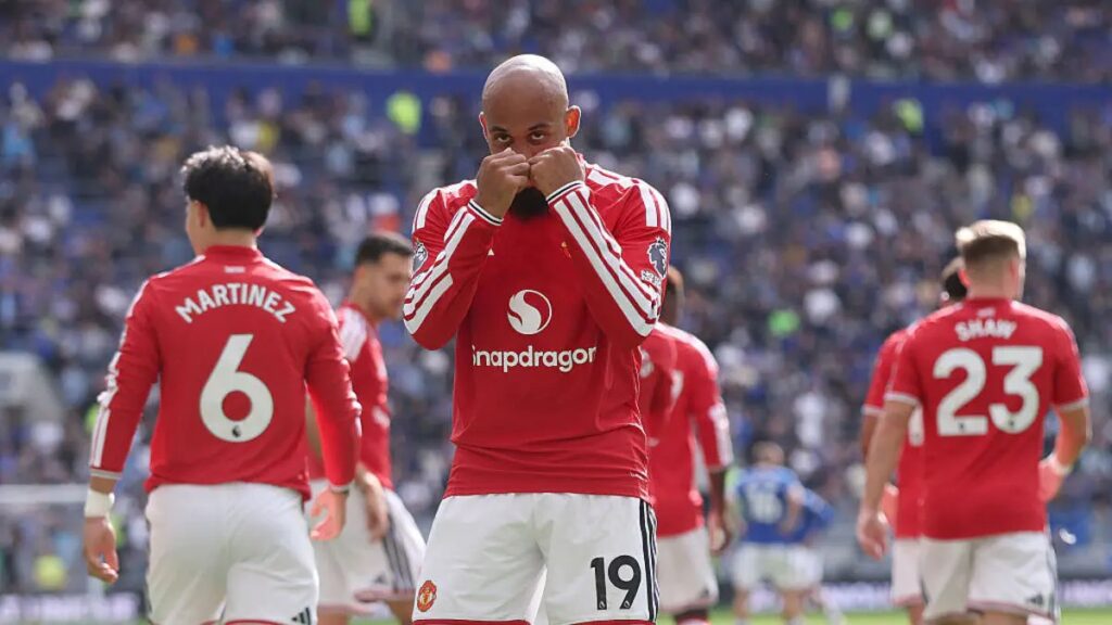Manchester United's Bryan Mbeumo (No. 19) stands with hands clasped over his face in a moment of frustration, with teammates Martínez (No. 6) and Shaw (No. 23) nearby and a packed stadium crowd blurred behind them