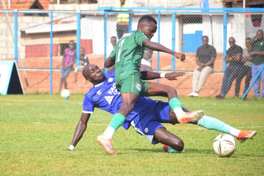 Police FC's Farouk Matovu makes a sliding tackle on Shafik Kakande as the ball breaks away, with spectators watching from behind the pitch fence.