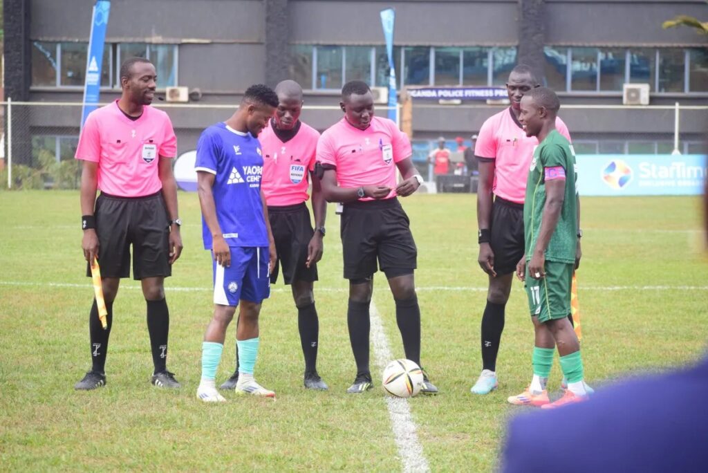 Police and UPDF team captains stand with match officials in pink at the centre circle for the coin toss before kickoff.