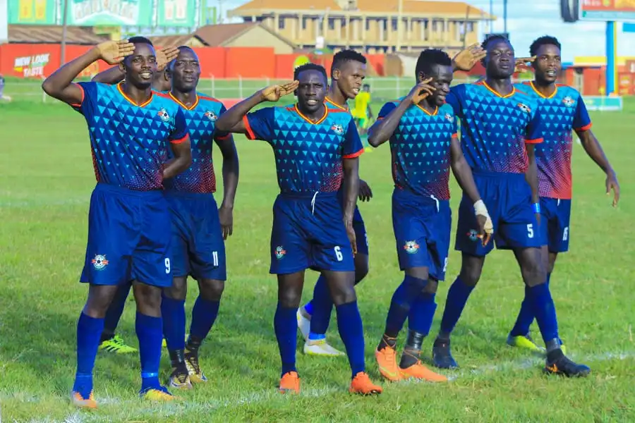 Archive photo of UPDF footballers in blue kits celebrating together with salute gestures on the pitch.