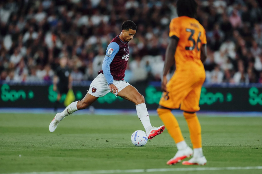 West Ham midfielder Divine Mukasa strikes the ball as a Wolves player closes him down.