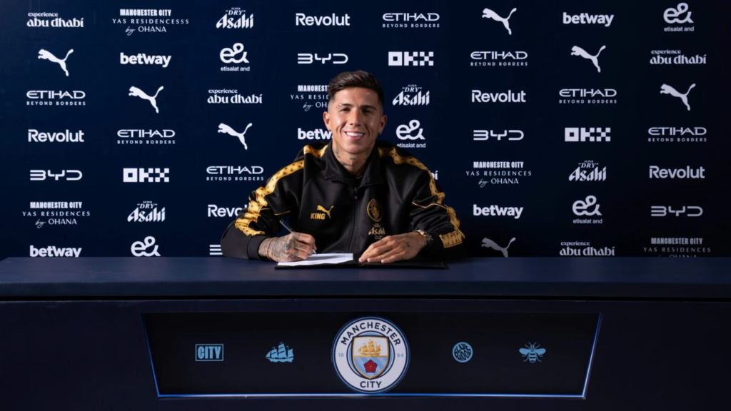 Enzo Fernández signs a contract beside the Manchester City crest.