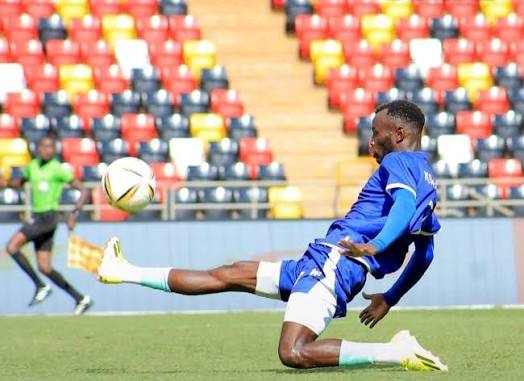 Police player in blue slides with one leg extended towards an airborne ball.