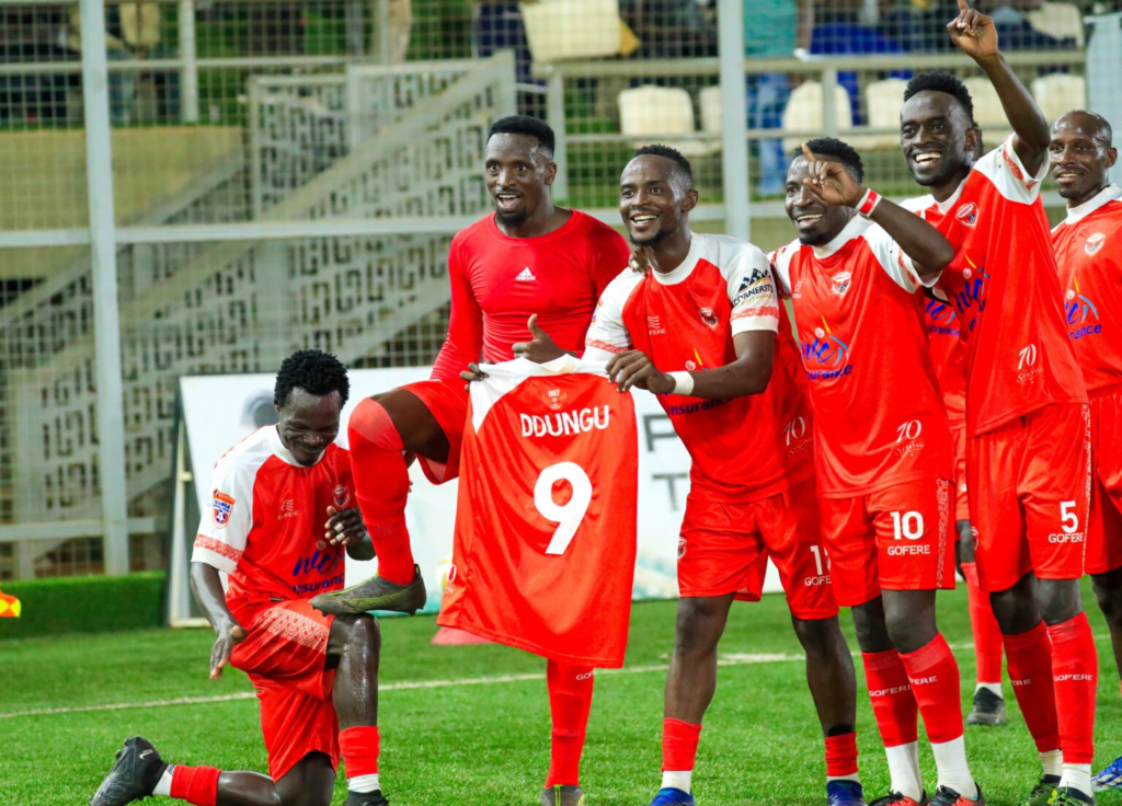 Rickman celebrates in a red undershirt while an Express teammate holds up his number nine jersey after his goal against KCCA