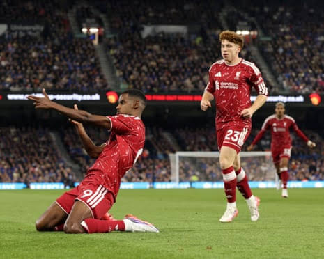 Liverpool's Alexander Isak celebrates on his knees with arms outstretched after scoring, as teammate runs toward him on the pitch.