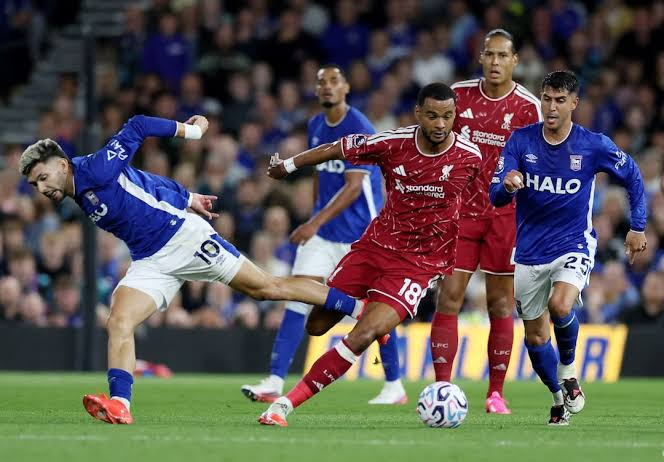 Liverpool's Cody Gakpo dribbles the ball past Ipswich Town defenders, with Virgil van Dijk following play in the background.