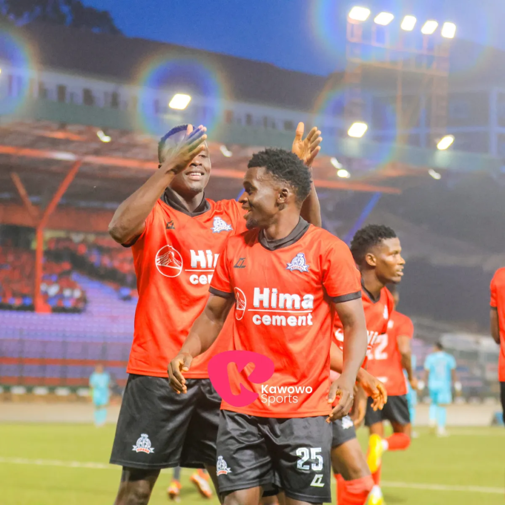 Vipers SC players Hilary Mukundane and AbdulKarim Watambala celebrate on the pitch during their CAF Champions League match, with teammates and stadium lights in the background.