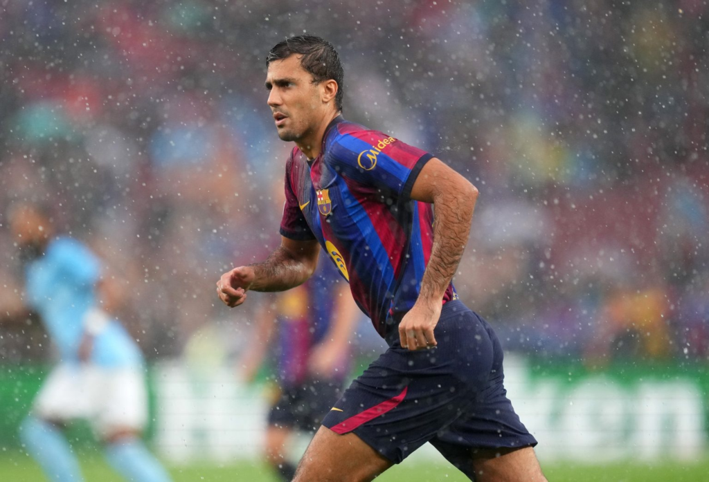 A Barcelona player in a blue-and-maroon kit running through heavy rain, an opposition player blurred in the background.