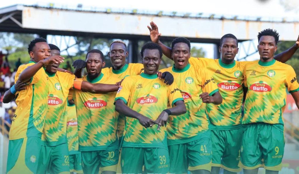 BUL FC footballers in yellow and green Fortune Butto-sponsored jerseys celebrate a goal together on the pitch, arms raised and fists clenched.