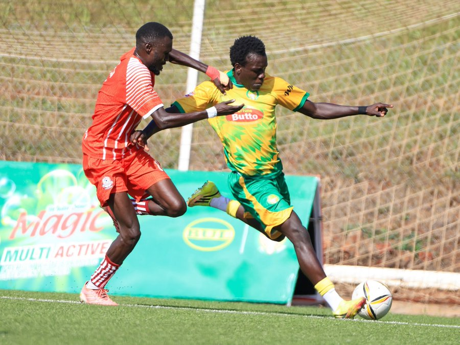 A BUL FC player in yellow and green surges past a Blacks Power defender in orange, controlling the ball near the byline in front of the goal net.