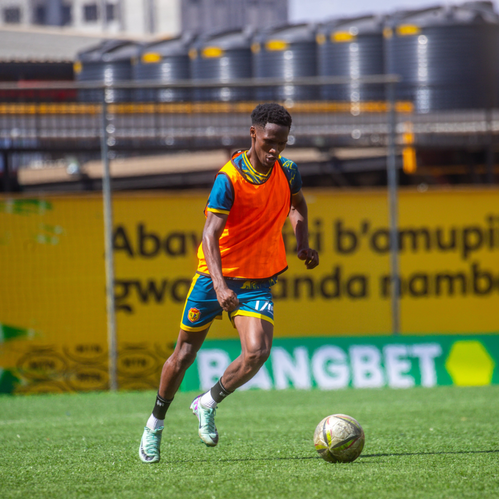KCCA FC player wearing an orange training bib controls a football on the pitch.