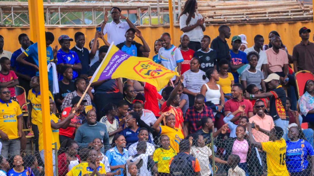 KCCA FC supporters cheering and waving a yellow club flag at MTN Omondi Stadium.