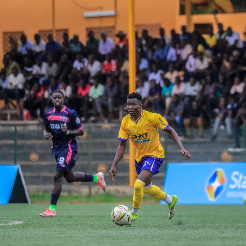 KCCA midfielder Ibrahim Kasule carries the ball forward as a Kataka FC player follows behind.