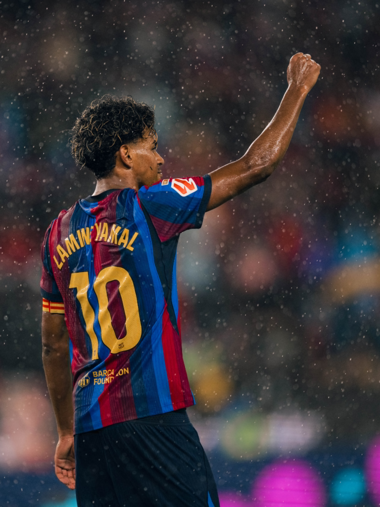 Barcelona winger Lamine Yamal celebrates with his right fist raised while wearing the number 10 shirt in heavy rain.